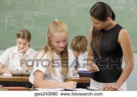 Female Teacher Teaching A Schoolgirl With Other Students Sitting In The Background Female Teacher Teaching A Schoolgirl With Other Students Sitting In The Background