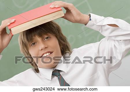 Portrait of a schoolboy holding a book over his head and smiling View Large Photo Image Picture - Portrait of a schoolboy holding a book over his head and smiling. Fotosearch