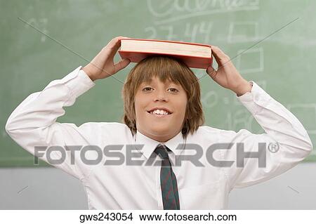 Portrait of a schoolboy holding a book over his head and smiling View Large Photo Image Picture - Portrait of a schoolboy holding a book over his head and smiling. Fotosearch