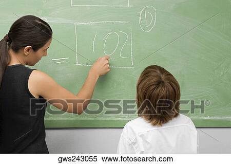 Rear view of a female teacher teaching a schoolboy in a classroom View Large Photo Image Stock Photography - Rear view of a female teacher teaching a schoolboy in a classroom. Fotosearch