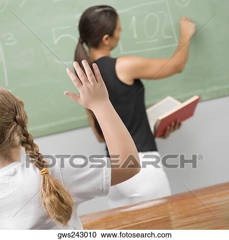 Stock Image - Rear view of a schoolgirl in a classroom with her hand raised. Fotosearch