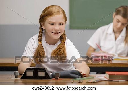 Schoolgirl sitting in a classroom and smiling View Large Photo Image Stock Image - Schoolgirl sitting in a classroom and smiling. Fotosearch