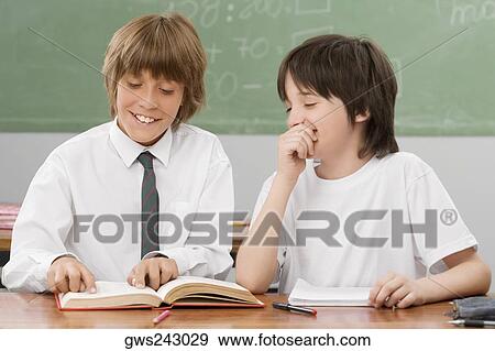 Two schoolboys reading a book together in a classroom and smiling View Large Photo Image Stock Photo - Two schoolboys reading a book together in a classroom and smiling. Fotosearch