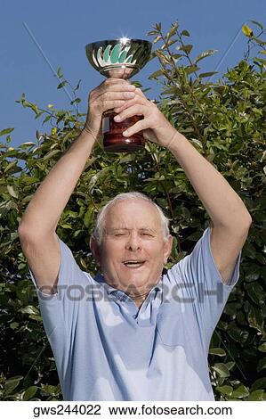 Senior man holding a trophy over his head View Large Photo Image Stock Image - Senior man holding a trophy over his head. Fotosearch