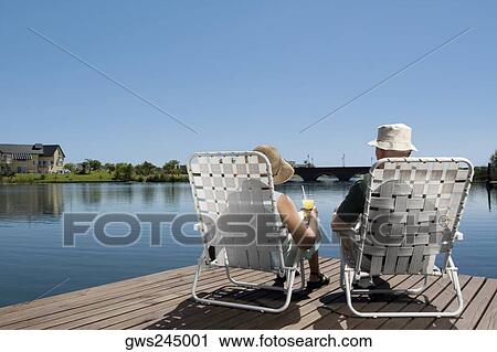 Stock Image - Rear view of a couple sitting on chairs at the boardwalk. Fotosearch