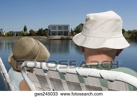 Rear view of a couple sitting on chairs at the lakeside View Large Photo Image Stock Image - Rear view of a couple sitting on chairs at the lakeside. Fotosearch