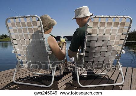 Stock Photo - Rear view of a senior couple sitting on chairs at the lakeside. Fotosearch
