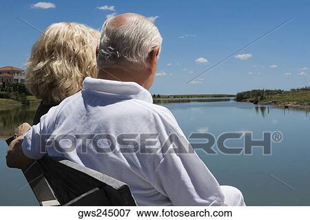 Stock Photo - Senior couple sitting on a bench at the lakeside. Fotosearch