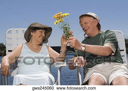 Stock Image - Senior man giving flowers to a senior woman and smiling. Fotosearch