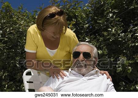 Senior man sitting on a chair with a senior woman standing behind him View Large Photo Image Stock Image - Senior man sitting on a chair with a senior woman standing behind him. Fotosearch