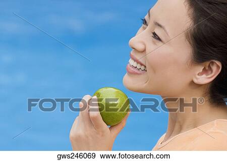 Side profile of a young woman holding an green apple View Large Photo Image Stock Photo - Side profile of a young woman holding an green apple. Fotosearch