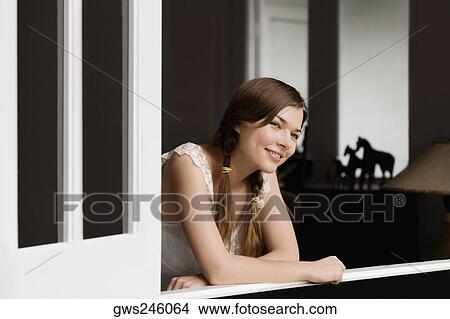 Picture - Young woman leaning on a window and smiling. Fotosearch
