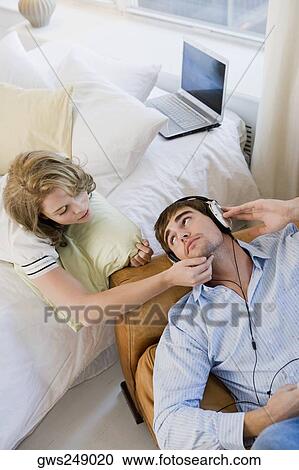 High angle view of a young man listening to music and a young woman lying on the bed beside him View Large Photo Image Stock Image - High angle view of a young man listening to music and a young woman lying on the bed beside him. Fotosearch