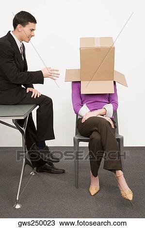 Businesswoman covering her face with a cardboard box and a businessman sitting beside her on a desk View Large Photo Image Stock Image - Businesswoman covering her face with a cardboard box and a businessman sitting beside her on a desk. Fotosearch