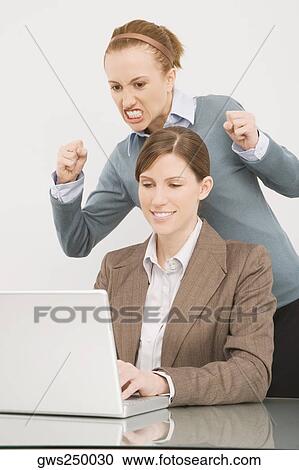 Businesswoman working on a laptop with her colleague clenching teeth behind her View Large Photo Image Stock Image - Businesswoman working on a laptop with her colleague clenching teeth behind her. Fotosearch