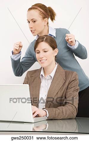 Businesswoman working on a laptop with her colleague clenching teeth behind her View Large Photo Image Stock Image - Businesswoman working on a laptop with her colleague clenching teeth behind her. Fotosearch