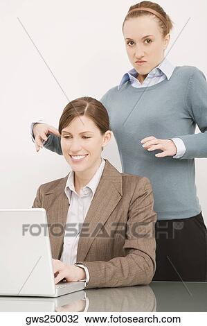 Businesswoman working on a laptop with her colleague try to strangling behind her View Large Photo Image Stock Image - Businesswoman working on a laptop with her colleague try to strangling behind her. Fotosearch