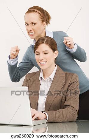 Businesswoman working on a laptop with her colleague clenching teeth behind her View Large Photo Image Stock Photo - Businesswoman working on a laptop with her colleague clenching teeth behind her. Fotosearch