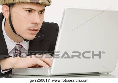 Close-up of a businessman wearing an army helmet and working on a laptop View Large Photo Image Stock Photo - Close-up of a businessman wearing an army helmet and working on a laptop. Fotosearch