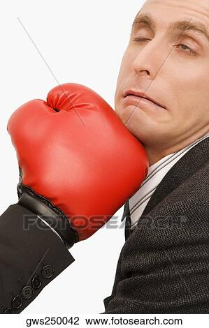 Stock Image - Close-up of a person's hand punching on a businessman's chin. Fotosearch