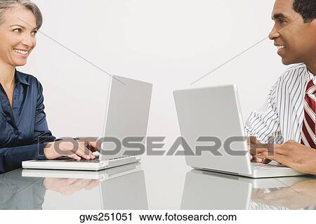 Stock Image - Businessman and a businesswoman working on laptops in an office. Fotosearch