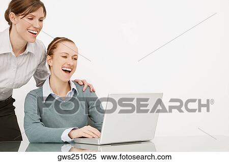 Stock Photography - Two businesswomen working on a laptop and smiling. Fotosearch