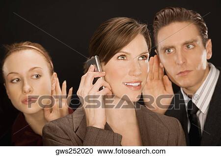 Businesswoman talking on a mobile phone with two business executives listening to her View Large Photo Image Stock Image - Businesswoman talking on a mobile phone with two business executives listening to her. Fotosearch