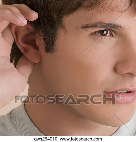Close-up of a young man listening View Large Photo Image Stock Image - Close-up of a young man listening. Fotosearch