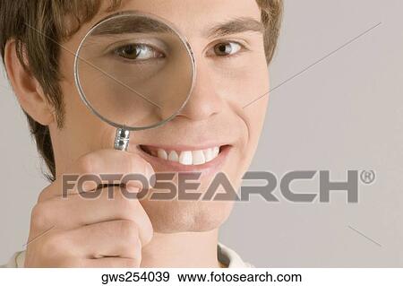 Close-up of a young man looking through a magnifying glass View Large Photo Image Stock Photo - Close-up of a young man looking through a magnifying glass. Fotosearch
