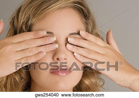 Stock Image - Close-up of a young woman covering her eyes with her hands. Fotosearch