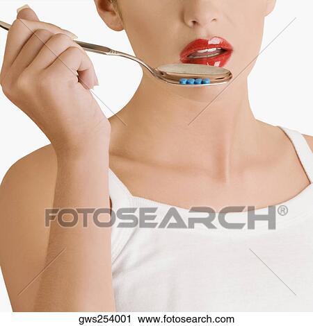 Stock Image - Close-up of a young woman holding pills in a spoon. Fotosearch
