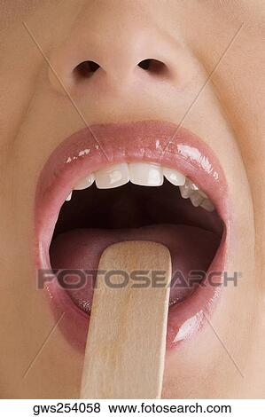 Stock Photo - Close-up of a young woman using a tongue depressor to examine her tongue. Fotosearch