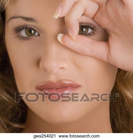 Stock Image - Portrait of a young woman looking through a circle formed by her fingers. Fotosearch