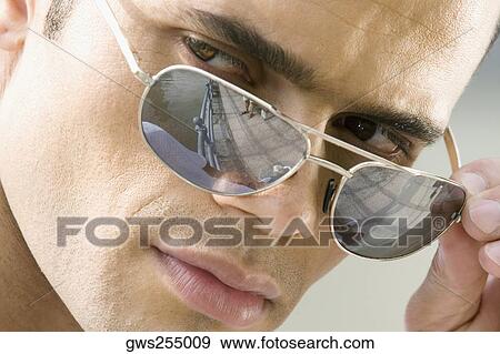 Close-up of a mid adult man peeking over his sunglasses View Large Photo Image Stock Photo - Close-up of a mid adult man peeking over his sunglasses. Fotosearch