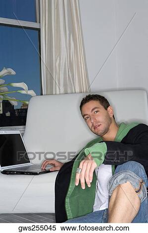 Portrait of a young man leaning against a couch and working on a laptop View Large Photo Image Stock Photography - Portrait of a young man leaning against a couch and working on a laptop. Fotosearch