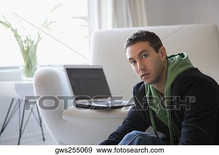 Portrait of a young man sitting with a laptop on a couch View Large Photo Image Stock Photo - Portrait of a young man sitting with a laptop on a couch. Fotosearch