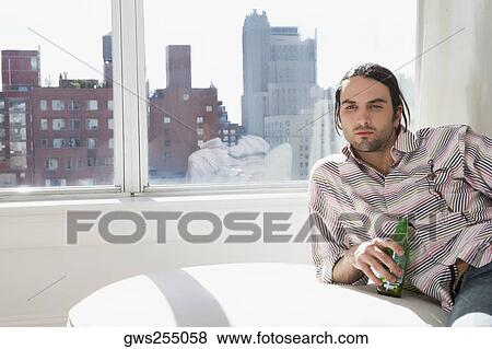 Young man lying on a couch and holding a beer bottle View Large Photo Image Stock Photo - Young man lying on a couch and holding a beer bottle. Fotosearch
