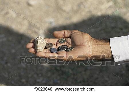 Stock Photo - Pakistan, Punjab, Taxila Valley, old coins and sculpted head in a hand. Fotosearch