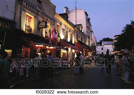 Stock Image - France, Paris, restaurants in a street of Montmartre, glimpse of the Sacré Coeur basilica. Fotosearch