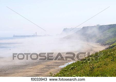 Stock Image - England, North Yorkshire, Sandsend, walkers on the beach. Fotosearch