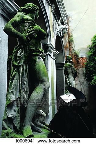 Stock Image - Italy, Venice, Masked man looking at statue. Fotosearch