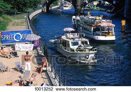 Stock Image - East part of the city, summer beach and tour boat on the Spree river. Fotosearch