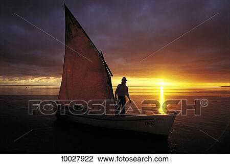 Stock Image - Mauritius, traditional fishing boat with sail at sunset. Fotosearch
