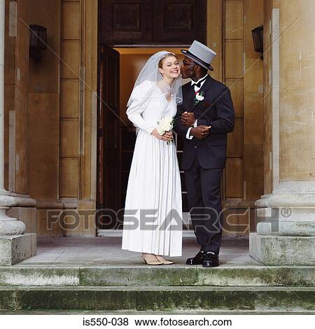 Stock Photo - Groom kisses bride outside church. Fotosearch