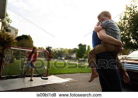 Adult carrying boy, girl playing hockey in background View Large Photo Image Stock Photo - Adult carrying boy, girl playing hockey in background. Fotosearch