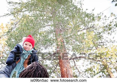 Stock Image - Baby boy being held up by father in forest. Fotosearch