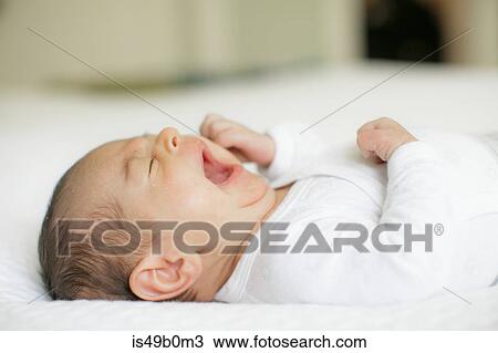 Stock Image - Baby boy, lying on bed, yawning, close-up. Fotosearch