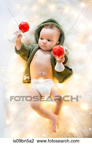 Stock Image - Baby boy lying on furry rug amongst decorative lights playing with rattles. Fotosearch