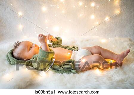 Stock Image - Baby boy lying on furry rug playing with decorative lights. Fotosearch