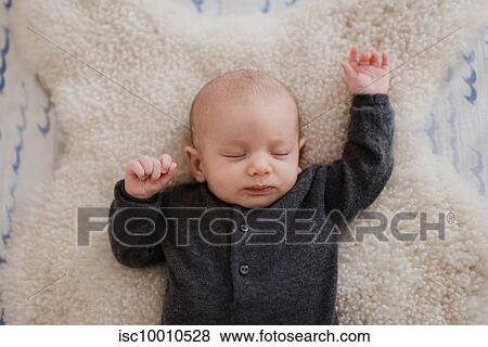 Stock Photo - Baby boy sleeping on sheepskin rug in crib, overhead view. Fotosearch